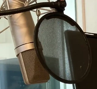 Schlankes Kondensatormikrofon auf einem Schreibtisch in einem modernen Aufnahmestudio, das mit Audioproduktionsgeräten ausgestattet ist.